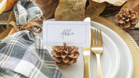 Place card with the name Abbie on it on white plates with gold utensil and a green, white and gray plaid napkin. Fall leaves as the centerpiece