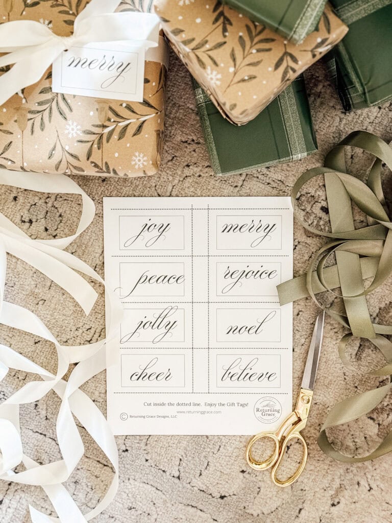 Gift wrapping scene with green and brown wrapped presents, white and green ribbons, gold scissors, and a sheet of holiday gift tags labeled “joy,” “merry,” “peace,” “rejoice,” “jolly,” “noel,” “cheer,” and “believe.”.