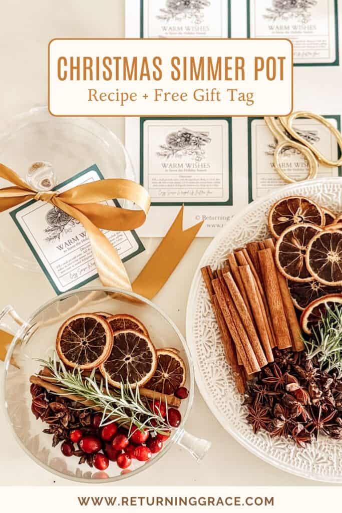 A white tray holds dried orange slices, cinnamon sticks, star anise, and cranberries beside a glass pot with similar ingredients. Gift tags, gold scissors, and a ribbon are also visible, with a Christmas simmer pot recipe sign above.