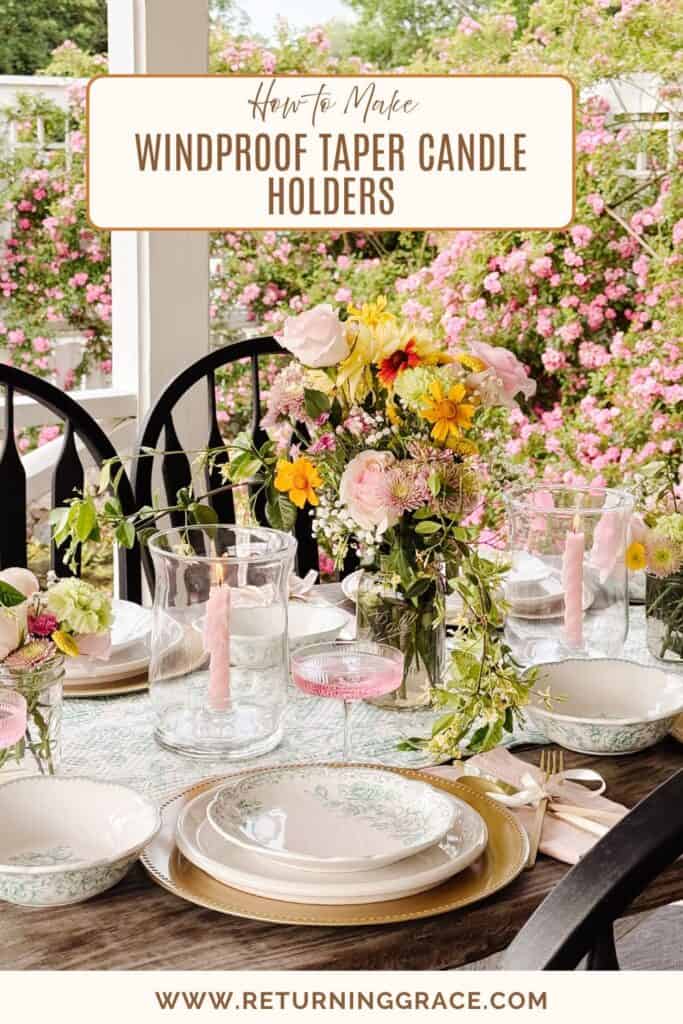 A beautifully set outdoor table features floral china, pink goblets, a lush bouquet of fresh flowers, and pink taper candles in DIY windproof taper candle holders, with blooming pink bushes and a white porch railing in the background.